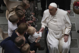 Pope Francis holds the hand of a toddler as he salutes faithful at the end of his weekly general audience in the Paul VI Hall, at the Vatican, Wednesday, Feb. 12, 2025.
